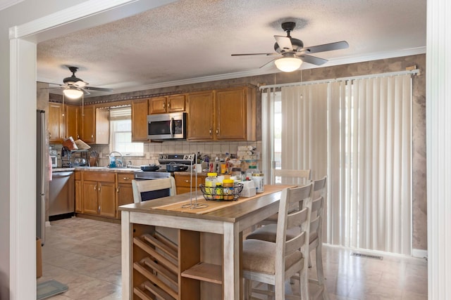 kitchen featuring a textured ceiling, decorative backsplash, appliances with stainless steel finishes, crown molding, and ceiling fan