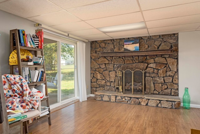 sitting room featuring wood-type flooring, a paneled ceiling, and a stone fireplace