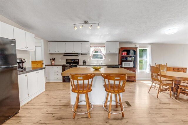 kitchen with a textured ceiling, black appliances, extractor fan, light wood-type flooring, and white cabinets