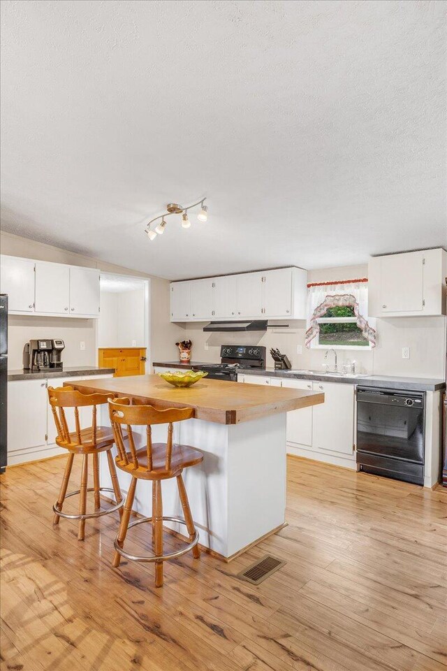 kitchen featuring a textured ceiling, black appliances, light wood-type flooring, and white cabinetry