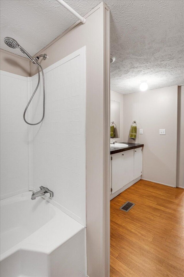 bathroom featuring vanity, a textured ceiling, hardwood / wood-style floors, and shower / tub combination