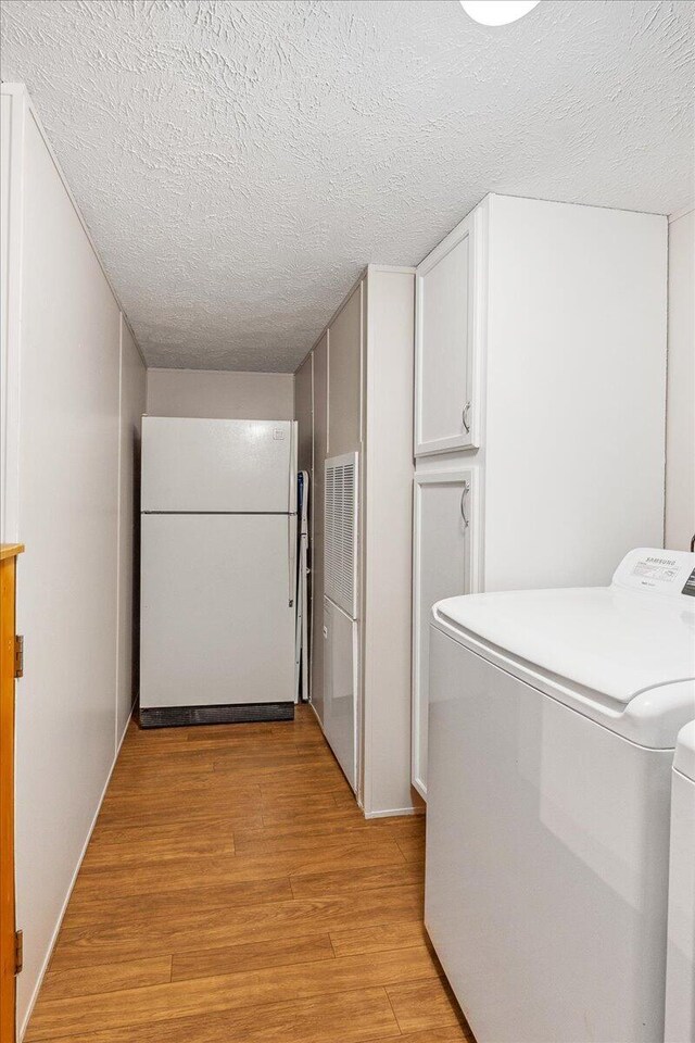 washroom featuring cabinets, light hardwood / wood-style floors, washer and clothes dryer, and a textured ceiling