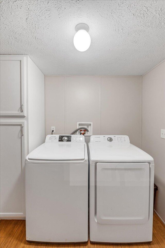 laundry room featuring a textured ceiling, washing machine and dryer, and light hardwood / wood-style floors