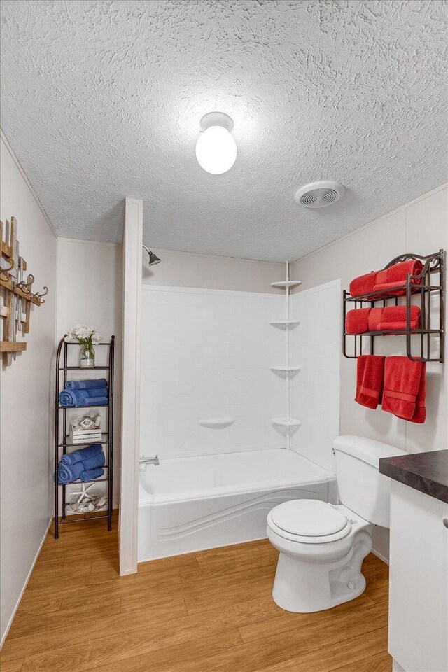 full bathroom featuring a textured ceiling, toilet, hardwood / wood-style floors, and shower / bath combination