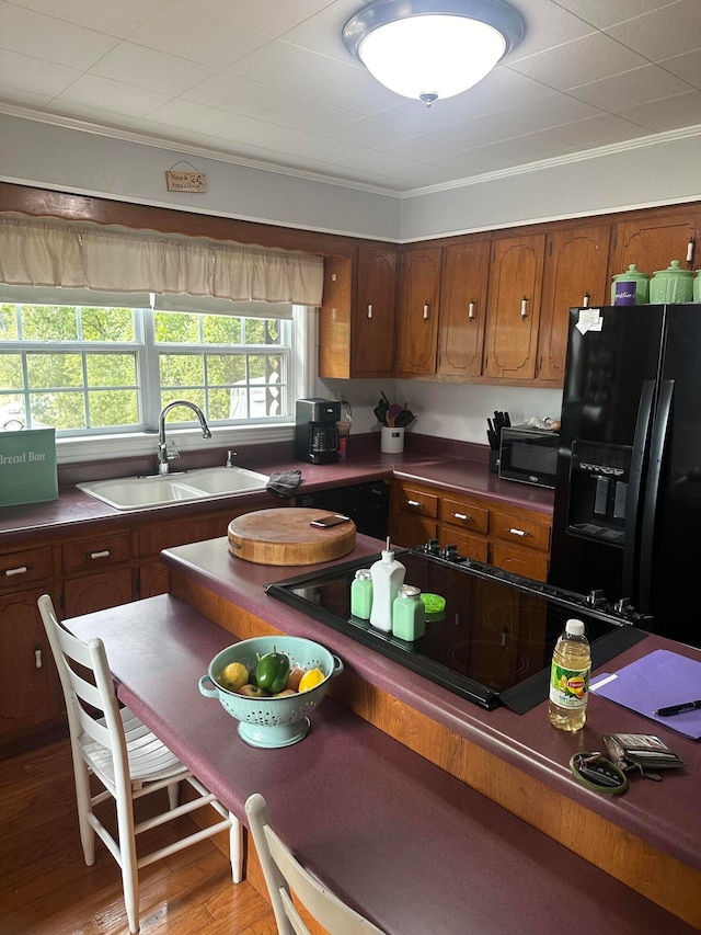 kitchen with black appliances, wood-type flooring, ornamental molding, and sink