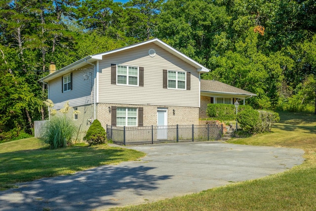 tri-level home featuring brick siding, fence, a front yard, a chimney, and driveway