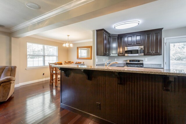 kitchen with a breakfast bar area, a notable chandelier, dark wood-type flooring, stainless steel appliances, and hanging light fixtures