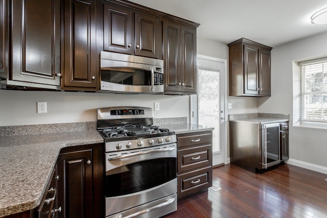 kitchen featuring wine cooler, dark brown cabinets, dark hardwood / wood-style flooring, stainless steel appliances, and light stone counters