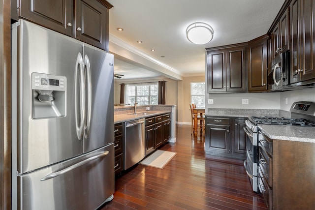 kitchen featuring dark brown cabinets, dark hardwood / wood-style flooring, appliances with stainless steel finishes, crown molding, and sink