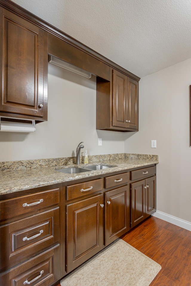 kitchen featuring dark wood-type flooring, light stone counters, a textured ceiling, and sink