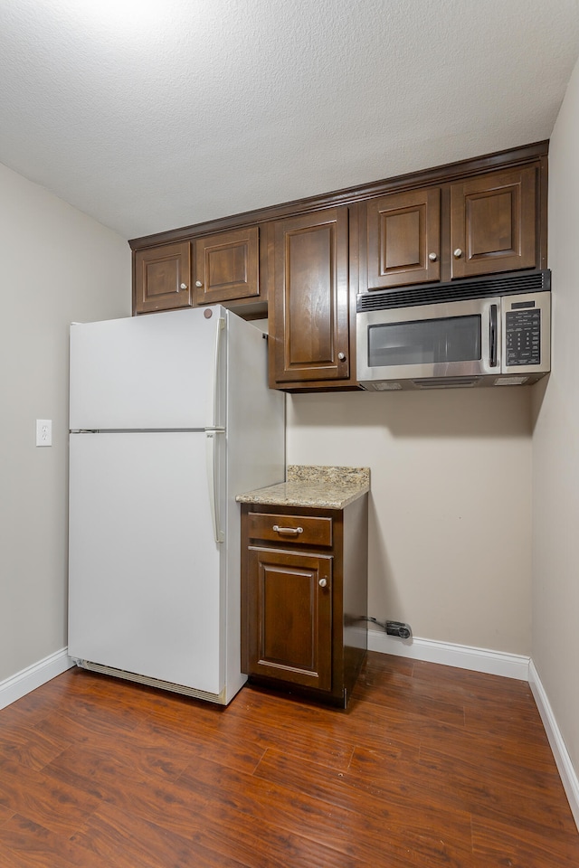 kitchen featuring white refrigerator, light stone countertops, dark hardwood / wood-style floors, dark brown cabinets, and a textured ceiling