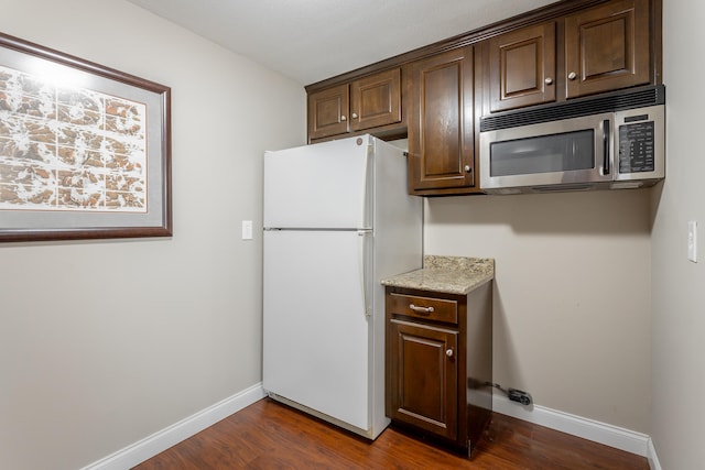 kitchen with white refrigerator, dark brown cabinetry, light stone countertops, and dark hardwood / wood-style floors