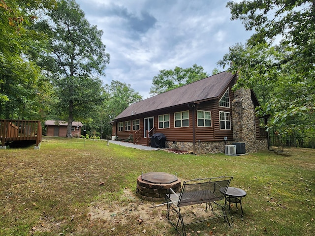 back of property with a wooden deck, cooling unit, a yard, and a fire pit