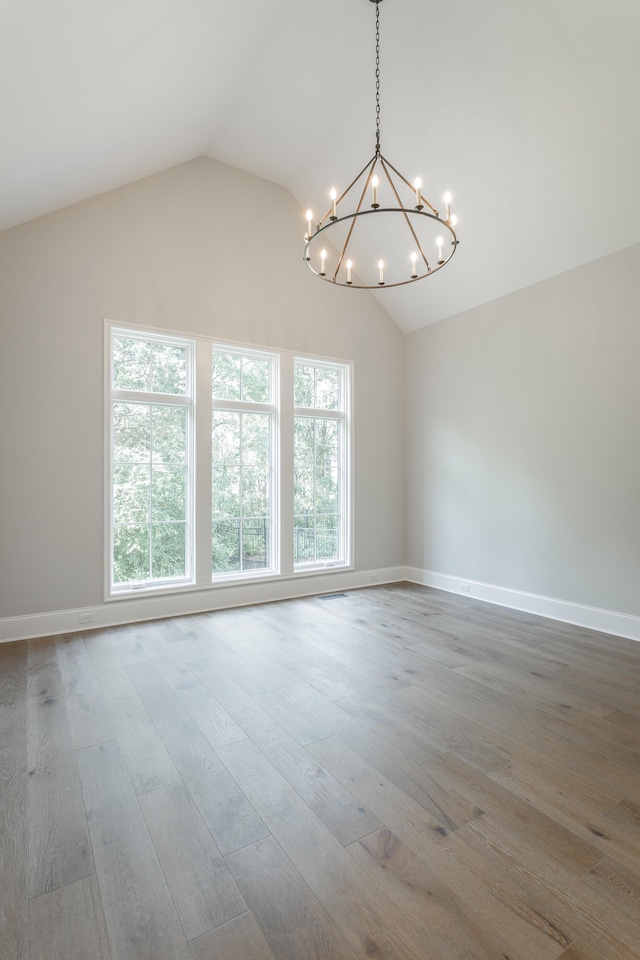 empty room featuring a notable chandelier, vaulted ceiling, and hardwood / wood-style floors