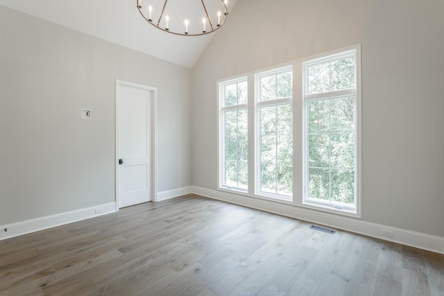 empty room with wood-type flooring, a notable chandelier, and plenty of natural light