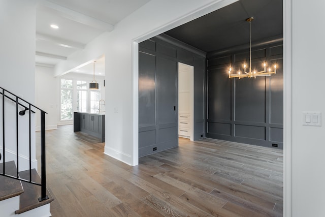 interior space with an inviting chandelier, wood-type flooring, and beam ceiling