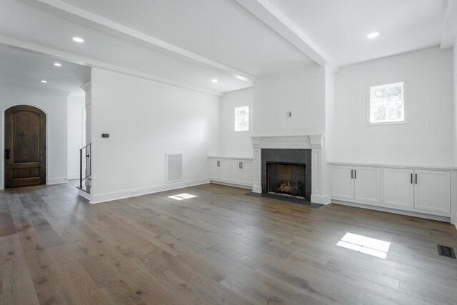 unfurnished living room featuring a premium fireplace, beamed ceiling, and hardwood / wood-style flooring