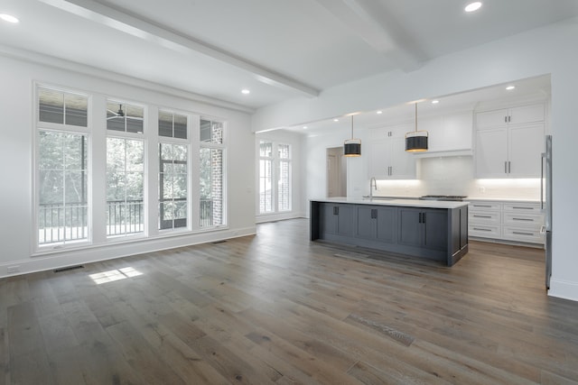 kitchen with hanging light fixtures, white cabinetry, beamed ceiling, and an island with sink