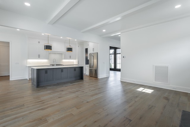 kitchen with stainless steel fridge, a kitchen island with sink, dark hardwood / wood-style floors, and white cabinets