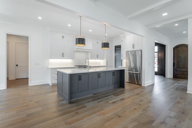 kitchen featuring high end refrigerator, white cabinetry, light hardwood / wood-style flooring, and an island with sink