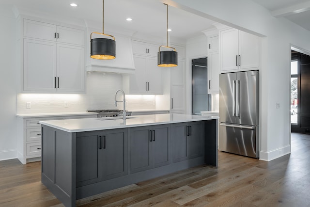 kitchen featuring a kitchen island with sink, high end fridge, hanging light fixtures, and white cabinetry