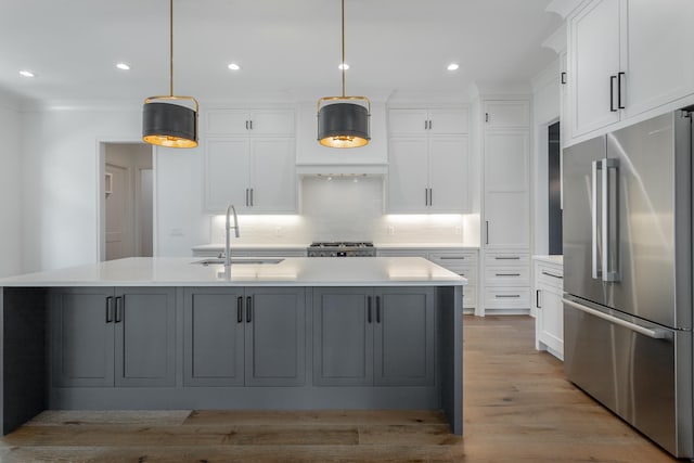 kitchen featuring pendant lighting, an island with sink, sink, appliances with stainless steel finishes, and light wood-type flooring