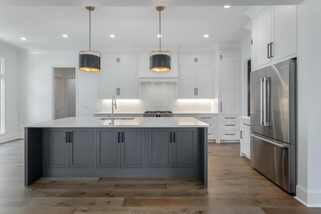 kitchen featuring sink, white cabinetry, hanging light fixtures, stainless steel appliances, and a center island with sink