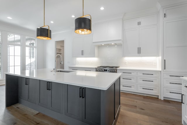 kitchen with white cabinets, a kitchen island with sink, hanging light fixtures, and sink