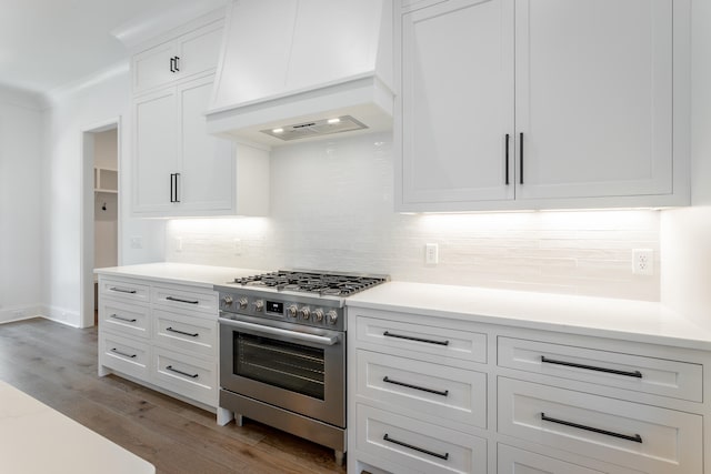 kitchen with light wood-type flooring, high end stove, tasteful backsplash, white cabinetry, and premium range hood