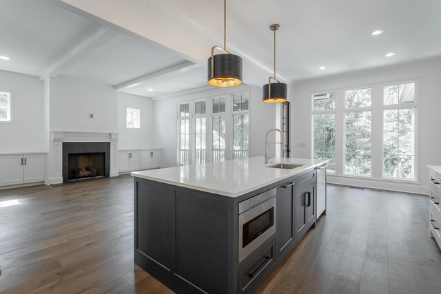 kitchen with gray cabinetry, an island with sink, stainless steel microwave, dark hardwood / wood-style flooring, and sink