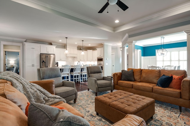 living room with hardwood / wood-style flooring, ceiling fan with notable chandelier, crown molding, and ornate columns