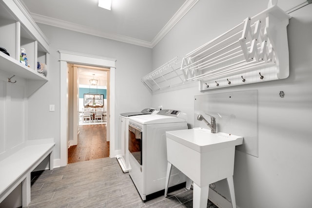 clothes washing area with ornamental molding, wood-type flooring, independent washer and dryer, and sink