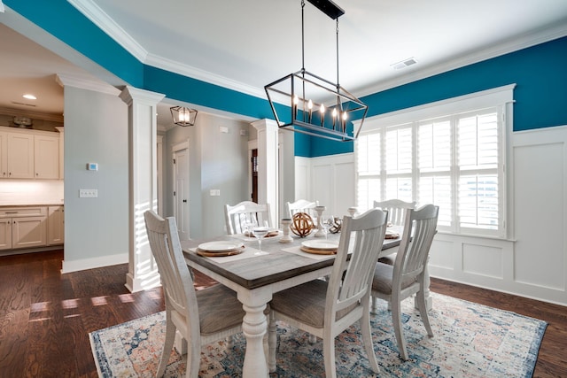 dining room featuring an inviting chandelier, dark wood-type flooring, crown molding, and ornate columns