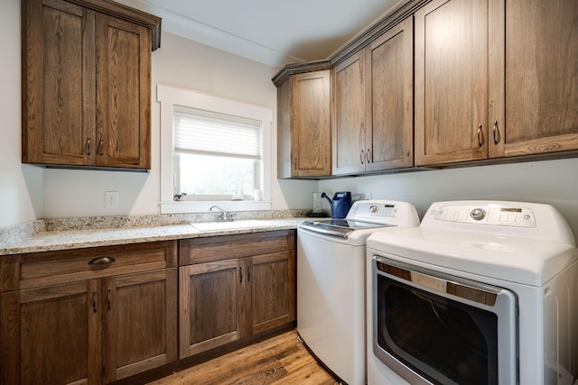 clothes washing area with separate washer and dryer, cabinets, light wood-type flooring, and sink