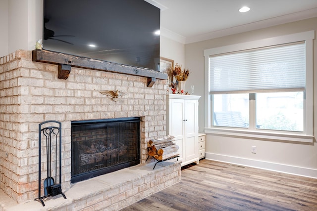 living room featuring light wood-type flooring, crown molding, ceiling fan, and a brick fireplace