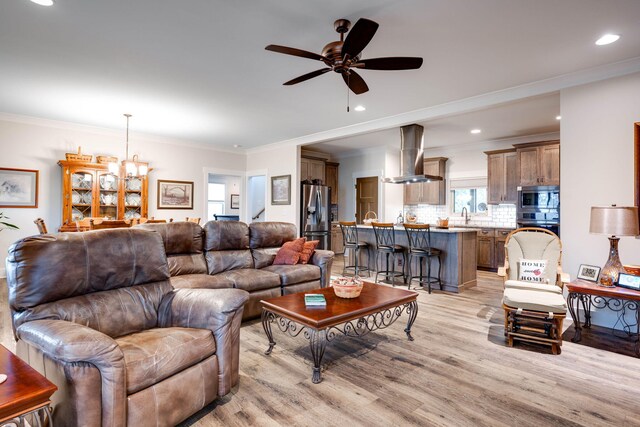 living room with ceiling fan with notable chandelier, light hardwood / wood-style floors, ornamental molding, and sink