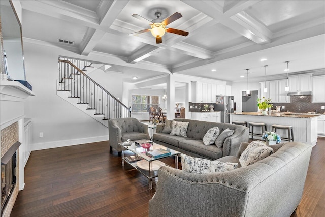 living room featuring coffered ceiling, beamed ceiling, a tiled fireplace, ceiling fan, and dark wood-type flooring