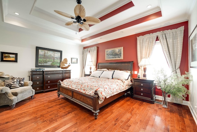 bedroom featuring ceiling fan, a tray ceiling, multiple windows, and hardwood / wood-style floors