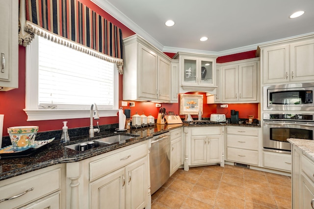 kitchen with appliances with stainless steel finishes, cream cabinetry, dark stone counters, and sink