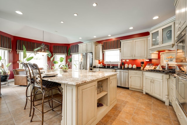 kitchen featuring appliances with stainless steel finishes, dark stone countertops, decorative light fixtures, a kitchen island with sink, and cream cabinets