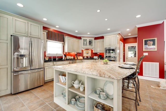 kitchen featuring sink, a kitchen island, cream cabinetry, stainless steel appliances, and dark stone counters