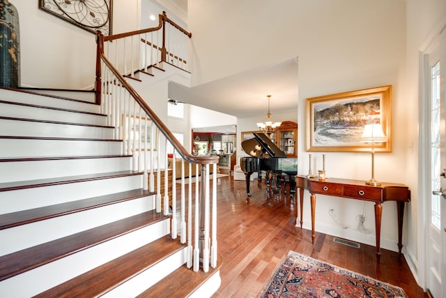 stairway featuring a notable chandelier, plenty of natural light, hardwood / wood-style floors, and a high ceiling