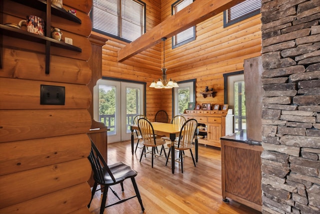 dining room with a chandelier, light wood-style flooring, rustic walls, and a towering ceiling