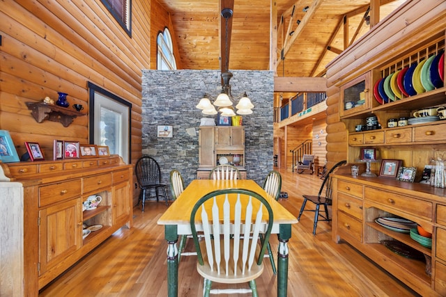 dining space with high vaulted ceiling, light wood-style floors, beamed ceiling, a notable chandelier, and rustic walls