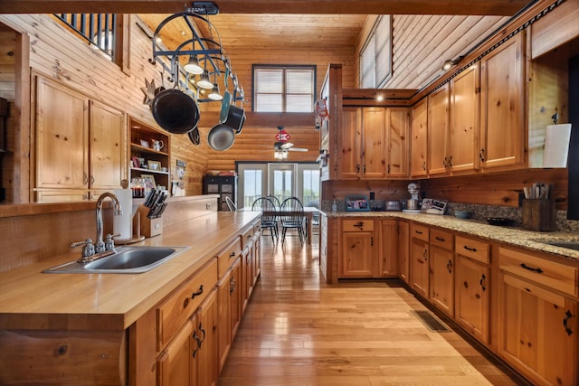 kitchen with wood ceiling, light wood-type flooring, rustic walls, high vaulted ceiling, and a sink