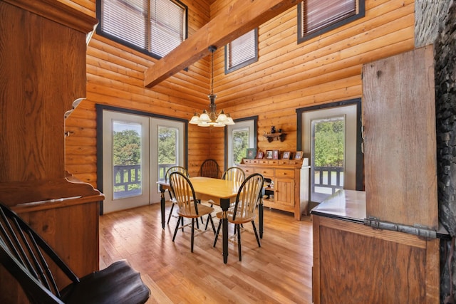 dining room featuring light wood finished floors, a notable chandelier, a towering ceiling, and log walls