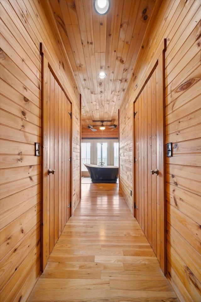 hallway with light wood finished floors, wooden walls, and wood ceiling