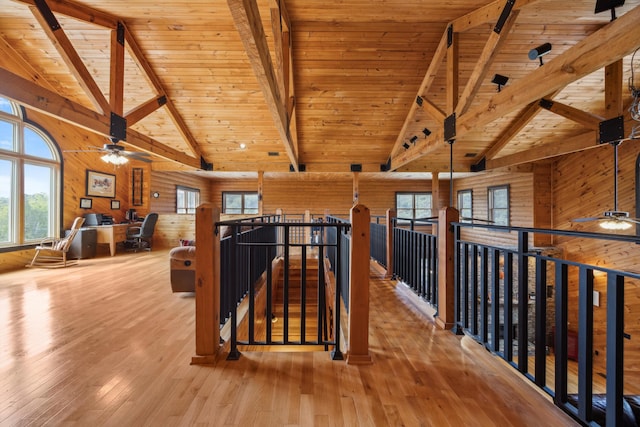 hallway with an upstairs landing, beam ceiling, wood walls, and hardwood / wood-style floors