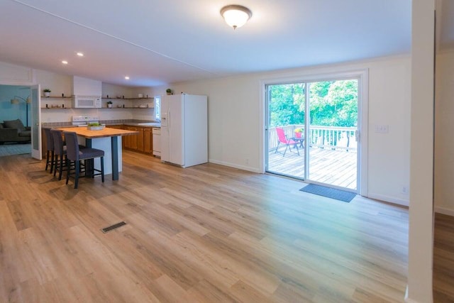 kitchen with butcher block countertops, white appliances, light hardwood / wood-style flooring, a kitchen bar, and a center island