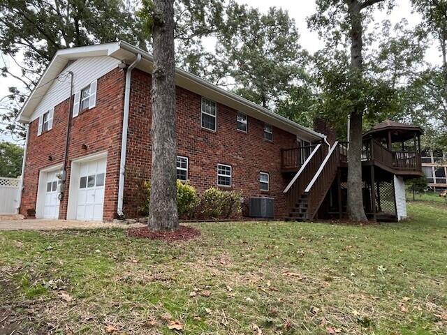 rear view of property featuring a deck, a yard, a garage, and central AC unit